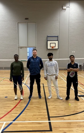 Group of students and a coach posing in the gym hall at Glasgow Kelvin College after a badminton session, standing on either side of the net. Group of students and a coach posing in the gym hall at Glasgow Kelvin College after a badminton session, standing on either side of the net.